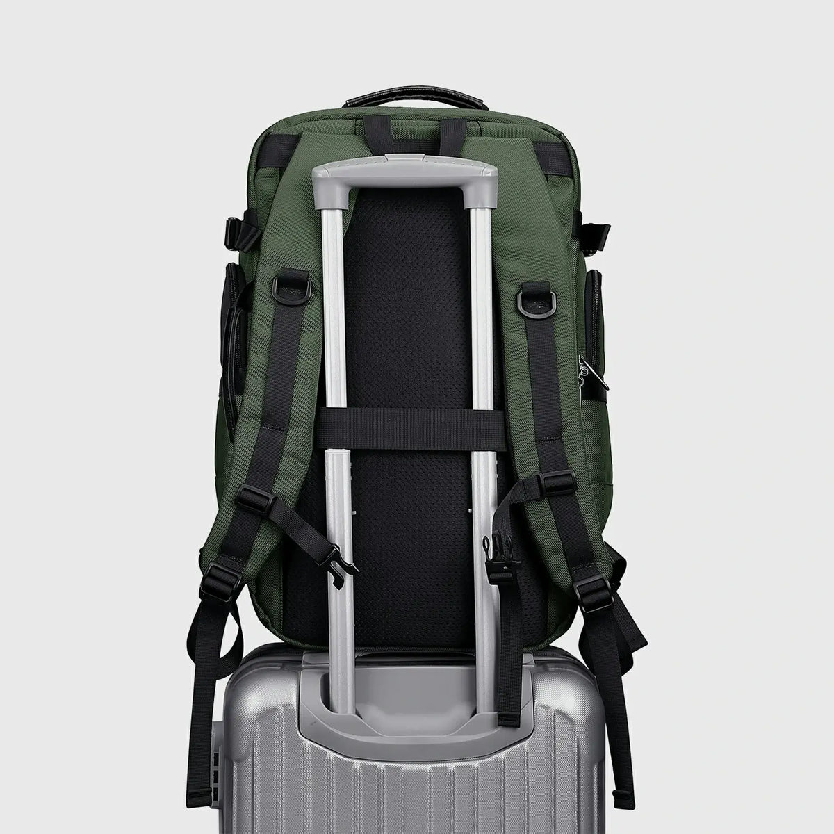 Army green carry on travel backpack secured to a suitcase with rear luggage strap