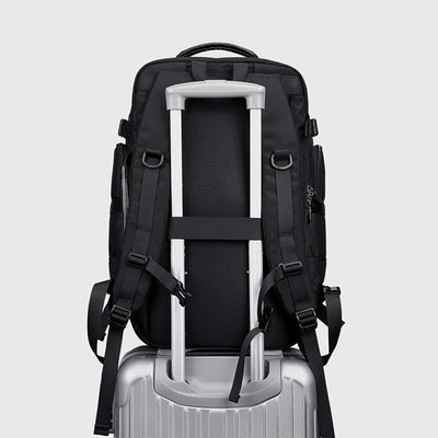 Black carry on travel backpack attached to rolling luggage with rear suitcase strap